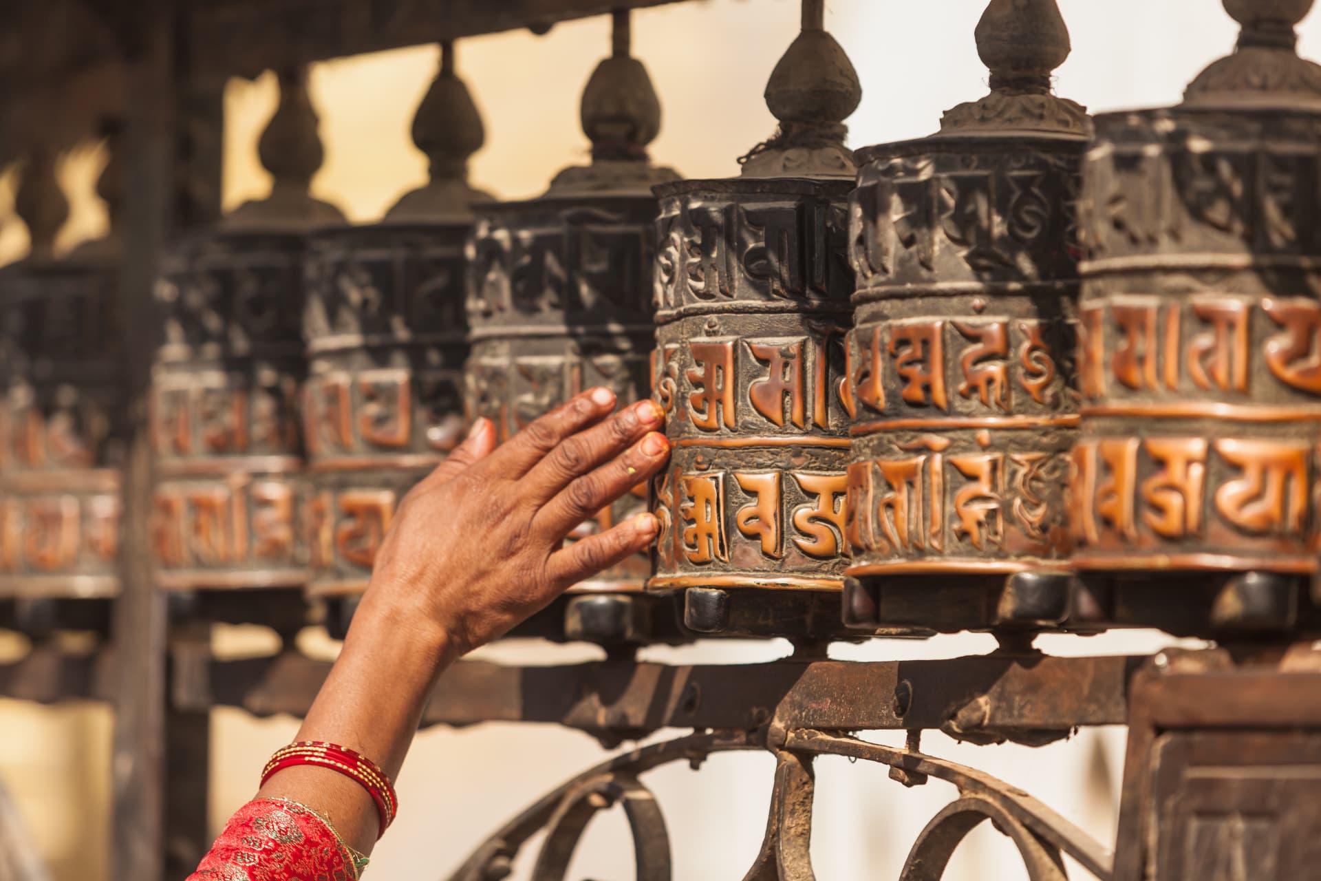 Hand dreht kupferne Gebetsmühlen an einem buddhistischen Tempel in Nepal