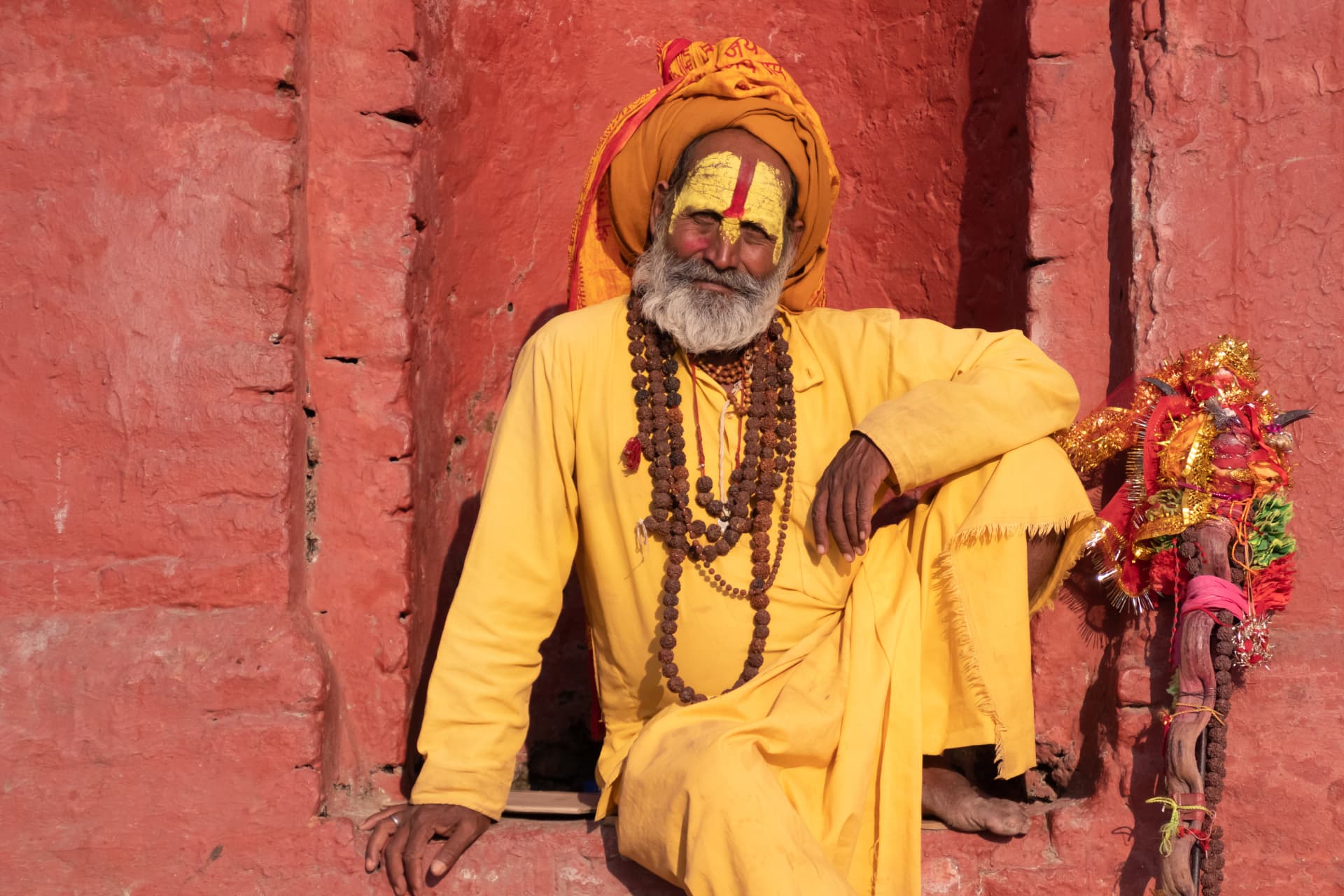 Sadhu in safrangelbem Gewand vor einer roten Tempelwand in Nepal